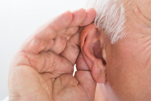 Older man trying to hear a noise with hand to ear